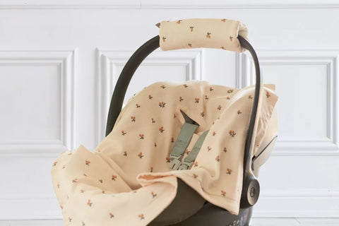 Eine Babyschale mit einem weichen, beigen Bezug mit kleinem Blumenmuster vor einer weißen, dekorativ getäfelten Wand.