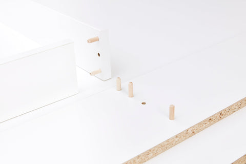 Nahaufnahme der weißen Flat-Pack-Teile mit Holzdübeln und Spanplattenkanten - perfekt für den Aufbau der KraftKids Wickelaufsatz weiß, passend für 160 cm breite HEMNES Kommode mit Blende, gerade Ausführung.