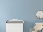 Ein KraftKids Wickelaufsatz weiß, passend für schmale 3er oder 4er Schubladen MALM Kommode, dient als praktische Wickelstation im Babyzimmer gegen eine hellblaue Wand. Daneben steht ein grauer Sessel mit weißem Fell und darüber ein runder Spiegel.