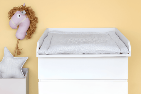 Ein KraftKids Wickelaufsatz weiß für schmale 3er/4er MALM Kommode steht an einer hellgelben Wand, mit einem weichen, gepunkteten Pad. Über dem Wickelplatz hängt ein Plüsch-Pferdekopf, daneben eine weiße Box mit Sternkissen in diesem gemütlichen Babyzimmer.