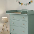 In einem sanft beleuchteten Zimmer steht eine mintgrüne Kommode mit vier Schubladen, auf der der KraftKids Wickelaufsatz XXL pastellgrün extra breit 108 cm mit Trennfach für HEMNES steht. Eine dreibeinige Lampe mit Sternenmuster und eine pastellfarbene Wimpelkette setzen charmante Akzente.