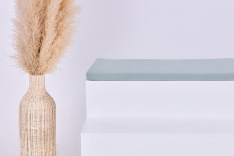 Eine Vase mit getrocknetem Gras steht neben einer weißen Treppe, ergänzt durch die KraftKids GmbH Sitzauflage für Ikea KALLAX 2er, 3er und 4er Regal in Musselin mint für einen gemütlichen Akzent in Ihrem Regalaufbau.