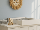 In einem Kinderzimmer stehen eine weiße Kommode mit dem KraftKids Wickelaufsatz weiß zum Quer-Wickeln für breite und schmale HEMNES Kommode, ordentlich gefaltete Handtücher, ein Holzspielzeugpferd und ein dekorativer Wandbehang mit Löwengesicht an der hellblauen Wand.