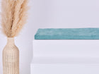 Eine geflochtene Vase mit Pampasgras steht neben einer KraftKids GmbH Sitzauflage für Ikea TROFAST Cord Breitcord Mint, gekrönt von einem gefalteten tealfarbenen Handtuch, vor einem schlichten hellen Hintergrund.