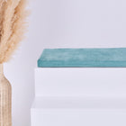 Eine geflochtene Vase mit Pampasgras steht neben einer KraftKids GmbH Sitzauflage für Ikea TROFAST Cord Breitcord Mint, gekrönt von einem gefalteten tealfarbenen Handtuch, vor einem schlichten hellen Hintergrund.