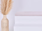 Eine große geflochtene Vase mit Pampasgras steht neben einem minimalistischen weißen Stufenpodest, gekrönt von der KraftKids GmbH Sitzauflage für Ikea TROFAST Cord Breitcord Beige Taupe, vor einem schlichten hellen Hintergrund.