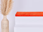Eine hohe geflochtene Vase mit Pampasgras steht neben einem weißen Stufenpodest, auf dem die KraftKids GmbH Sitzauflage für Ikea TROFAST Cord Breitcord Orange Reinorange steht, alles vor einem schlichten weißen Hintergrund.