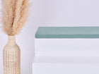 Eine hohe geflochtene Vase mit beigem Pampasgras steht neben weißen Stufen, auf denen die KraftKids GmbH Sitzauflage für Ikea TROFAST Doppelkrepp Grün Jade steht, vor einem schlichten hellen Hintergrund.
