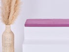Eine hohe geflochtene Vase mit beigem Pampasgras steht neben weißen Stufen, die oberste Stufe wird von einer gefalteten KraftKids GmbH Sitzauflage für Ikea TROFAST Musselin purpur aus doppellagigem Musselin in zartem Lila gekrönt.