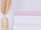 Eine hohe geflochtene Vase mit beigem Pampasgras steht neben einer modernen weißen Bank mit der KraftKids GmbH Sitzauflage für Ikea TROFAST Doppelkrepp Rosa vor einem schlichten weißen Hintergrund.