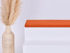 Eine hohe geflochtene Vase mit Pampasgras steht neben einem weißen Stufenpodest, auf dem das KraftKids GmbH Sitzauflage für Ikea TROFAST Doppelkrepp Rot Herbstrot Kissen liegt, alles vor einem schlichten hellen Hintergrund.