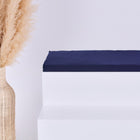 Eine hohe geflochtene Vase mit beigem Pampasgras steht neben einem weißen Stufenpodest, auf dem das KraftKids GmbH Sitzauflage für Ikea TROFAST Musselin dunkelblau Kissen liegt, vor einem schlichten hellen Hintergrund.