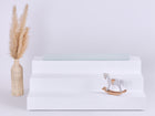 Ein weißer, dreistöckiger Ständer hält eine neuwertige Pusteblumen Sitzauflage für Ikea TROFAST von KraftKids GmbH, mit einer beigen Vase mit Pampasgras links und einem kleinen hölzernen Schaukelpferd unten rechts; der Hintergrund ist schlicht und hell.