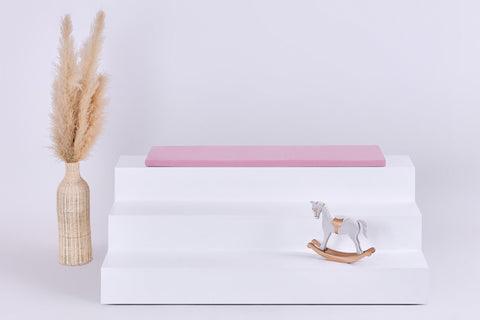 Die KraftKids GmbH Sitzauflage für Ikea TROFAST Musselin rosa verfügt über einen rosafarbenen, doppellagigen Musselinbezug mit weichem Schaumstoffkern, der perfekt zu Ihrem Regal passt. Für zusätzlichen Charme sorgt ein niedliches weißes Pferdespielzeug.