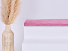 Eine hohe geflochtene Vase mit getrocknetem Pampasgras steht neben einer weißen stufenartigen Struktur, die mit der KraftKids GmbH Sitzauflage für Ikea TROFAST Cord Breitcord Rosa gekrönt ist, vor einem schlichten hellen Hintergrund.
