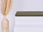 Eine hohe geflochtene Vase mit getrocknetem Pampasgras steht auf einem minimalistischen weißen Stufenpodest, das mit dem Kissen KraftKids GmbH Sitzauflage für Ikea TROFAST Doppelkrepp Grün Herbstgrün vor einem schlichten hellen Hintergrund versehen ist.