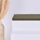 Eine hohe geflochtene Vase mit getrocknetem Pampasgras steht auf einem minimalistischen weißen Stufenpodest, das mit dem Kissen KraftKids GmbH Sitzauflage für Ikea TROFAST Doppelkrepp Grün Herbstgrün vor einem schlichten hellen Hintergrund versehen ist.