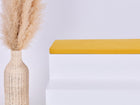 Eine hohe geflochtene Vase mit beigem Pampasgras steht neben einem weißen Stufenpodest, das mit der KraftKids GmbH Sitzauflage für Ikea TROFAST Doppelkrepp Gelb Senf vor einem schlichten hellen Hintergrund gekrönt wird.