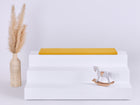 Ein weißer, dreistöckiger Aufsteller mit einer KraftKids GmbH Sitzauflage für Ikea TROFAST Doppelkrepp Gelb Senf auf der oberen Etage, einer dekorativen Vase mit getrocknetem Pampasgras auf der linken Seite und einem kleinen Holzschaukelpferd auf der unteren Etage.