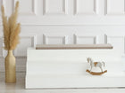 Ein minimalistisches Interieur mit weiß getäfelten Wänden, einer weißen Stufenbank mit der KraftKids GmbH Sitzauflage für Ikea TROFAST Musselin beige, einem dekorativen Holzschaukelpferd und einer hohen geflochtenen Vase mit getrocknetem Pampasgras.