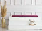 Ein minimalistisches Interieur mit einer hohen Vase mit Pampasgras, einer weißen Stufenbank mit der KraftKids GmbH Sitzauflage für Ikea TROFAST Leinen magenta dunkel und einem kleinen Holzschaukelpferd vor einer weiß getäfelten Wand.