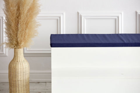 Eine hohe geflochtene Vase mit Pampasgras steht neben einer weißen Bank mit der KraftKids GmbH Sitzauflage für Ikea KALLAX Regal in Leinen blau dunkelblau, alles vor einer weißen Wand mit Zierleiste.