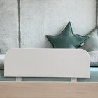 Ein minimalistisches und sicheres Kinderbett mit blassgrüner und weißer Bettwäsche, zwei großen sternförmigen Kissen und dem KraftKids Bettschutzgitter Rausfallschutz in weiß für sicheren Schlaf, vor einer hellen Betonwand.