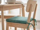 Ein heller Holzstuhl mit einem grünen KraftKids Sitzkissen für Stühle aus Breitcord ist an der Sitzfläche befestigt. Er steht neben einem passenden Tisch mit einer Schüssel und einem Geschirrtuch in einer hellen, minimalistischen Küche.
