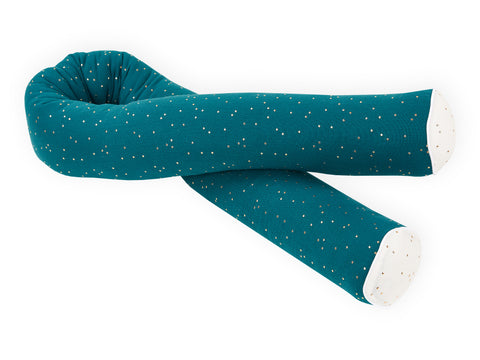 Das KraftKids Wickeltischumrandung Musselin goldene Punkte auf Petrol ist ein tealfarbenes zylindrisches Körperkissen mit goldenen Punkten und cremefarbenen Enden, das in einer S-Form vor einem weißen Hintergrund gewickelt ist.