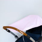 Nahaufnahme eines Kinderwagens mit hellrosafarbenem Verdeck mit dem KraftKids Sonnensegel "weiße Punkte auf Rosa" und einem braunen Lenker vor einem schlichten hellgrauen Hintergrund.