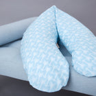 Das KraftKids Stillkissen "qualitäts Stillkissen weiße Pfeile auf Blau" mit ergonomischer Form liegt auf einer hellblauen Polsterbank mit Holzbeinen vor grauem Hintergrund.