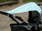 Nahaufnahme eines Kinderwagens mit dem Sonnensegel "weiße Pfeile auf Mint" von KraftKids, der leichten Schatten spendet. Der Hintergrund im Freien ist leicht verschwommen.
