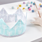 Eine handgenähte Stoffkrone von KraftKids mit weißem Pfeilmuster auf Mint liegt auf einer weißen Fläche. Im Hintergrund sorgen ein Stern-Zauberstab und eine bunte Filzkugel-Girlande für die perfekte Kinderparty-Stimmung.