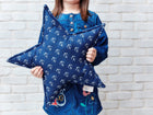 Ein Kind in einem blauen Kleid hält das KraftKids Sternkissen weiße Anker auf Dunkelblau, ein anpassbares Accessoire für Kinderzimmer, vor einer weißen Backsteinwand.