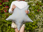 Ein Kind in weißem Langarmshirt und geblümten Shorts hält das KraftKids Sternkissen "goldene Linien auf Grau" in der Hand und steht im Freien vor Grün - die perfekte Inspiration für jedes stilvolle Kinderzimmer.