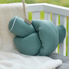 Die KraftKids Wickeltischumrandung Musselin nilblau, ein weiches grünes Kissen für den Einsatz als Bettschlange oder Kantenschutz Wickelkommode, liegt auf einer cremefarbenen Vliesdecke auf einer grauen Bank mit weißem Geländer, die im Freien auf grünem Gras steht.