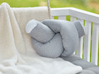 Ein KraftKids Wickeltischumrandung Musselin grau Punkte liegt auf einem weißen Kinderbett mit grauen Polstern und Latten, neben einer weichen cremefarbenen Decke, mit einem verschwommenen grünen Hintergrund, der von außen sichtbar ist.