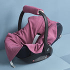 Eine marineblaue Babyschale mit schwarzem Griff wird von der KraftKids Babydecke für Babyschale Sommer Musselin purpur bedeckt, die auf einem minimalistischen hellblauen Hintergrund mit geometrischen Stufen steht.