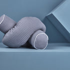 Eine graue, strukturierte Wickeltischumrandung Waffel Piqué von KraftKids mit weißer Paspel ist knotenförmig angeordnet und ruht auf einer blauen geometrischen Fläche und Hintergrund.