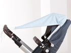 An einem dunkelgrauen Kinderwagen ist ein KraftKids Sonnensegel weiße Feder Muster auf Blau angebracht, das vom Griff bis zur Sitzfläche reicht und Schatten spendet. Der Kinderwagen mit dem Baldachin steht in einem Innenraum in der Nähe einer weißen Wand.