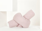 Die KraftKids Wickeltischumrandung Musselin mit goldenen Punkten auf Rosa, weich und in Knotenform, liegt auf weißem Untergrund mit minimalistischen weißen geometrischen Formen im Hintergrund.