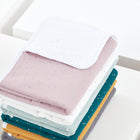 Ein ordentlich gefalteter Stapel weicher, bunter Babydecken und die KraftKids Wickelunterlage Musselin goldene Punkte auf Rosa ruht auf einer weißen Fläche. Die oberste rosa Decke zeigt ihre strukturierte Unterseite mit dezenten goldenen Punkten.