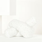 Das KraftKids Wickeltischumrandung Musselin goldene Punkte auf Weiß, ein weiches weißes Kissen mit goldenen Punkten, liegt auf einer weißen Fläche zwischen minimalistischen geometrischen Formen.