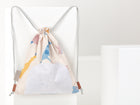 Der KraftKids Turnbeutel Musselin Zoe's Dinosaurier auf Beige hängt auf einem weißen Sockel. Dieser Rucksack mit Kordelzug hat einen beigen Stoff mit Dinosaurier-Aufdruck, hellgraue Träger, eine weiße Fronttasche mit schwarzen Punkten und lederbetonte Kordelzüge.