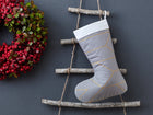 Eine KraftKids Weihnachtssocke "goldene Linien auf Grau" hängt an einer rustikalen Holzleiter neben einem festlichen Kranz - die perfekte Weihnachtsdeko für die Saison.