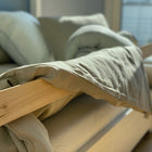 Ein ordentlich gemachtes Bett mit dem KraftKids Bettwäscheset Leinen Natur Braun, kuscheligen Kissen, einem Holzrahmen und einfallendem Sonnenlicht schafft eine einladende Atmosphäre.