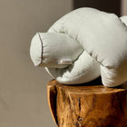 Eine Wickeltischumrandung Leinen in leicht grünem Weiß von KraftKids liegt auf einer polierten Holzschemel vor einer beigen Wand, sanft beschienen vom Sonnenlicht.