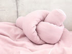 Ein weiches, rosafarbenes Knotenkissen liegt auf dem KraftKids Wickeltischumrandung Doppelkrepp Rosa vor einem hellgrauen Betonwandhintergrund.