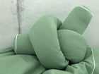 Eine Nahaufnahme des KraftKids Wickeltischumrandung Doppelkrepp Grün Jade, ein zartes grünes Kissen mit weißer Paspel, geformt wie ein großer Knoten und vor einem hellgrauen Hintergrund.