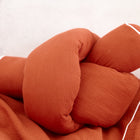 Die KraftKids Wickeltischumrandung Doppelkrepp Rot Herbstrot ist ein weiches, rostfarbenes Kissen mit weißer Paspelierung, das als verspielte Bettrolle gestaltet ist und auf einem passenden Stoff liegt.